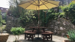 Et træbord udendørs med en gul parasol, omgivet af krukker med planter.