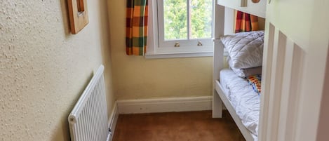 Una habitación pequeña y acogedora con una cama litera, un radiador, una ventana con cortinas y una puerta.