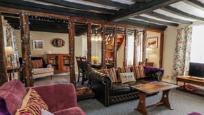 A cozy living room with a fireplace, a sofa, a coffee table, and a bookshelf. - Penlone Cottage (Rhayader)