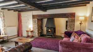 A cozy living room with a fireplace, a leather sofa, a purple rug, and a wooden table. - Penlone Cottage (Rhayader)