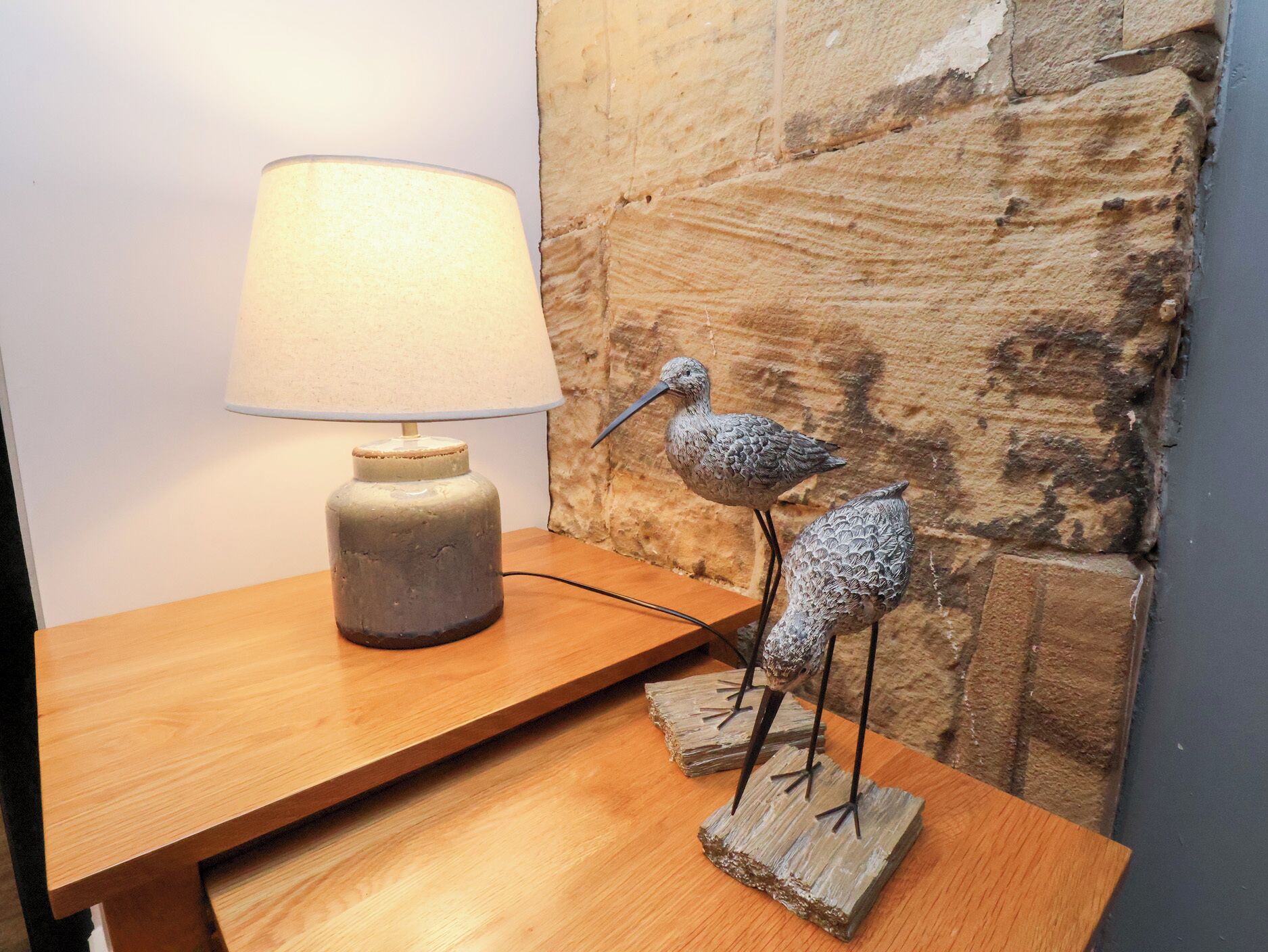 A wooden table with a lamp and two bird sculptures.