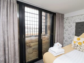 Quarto de hotel com uma cama, janela com vista para um edifício e porta com painel de vidro.