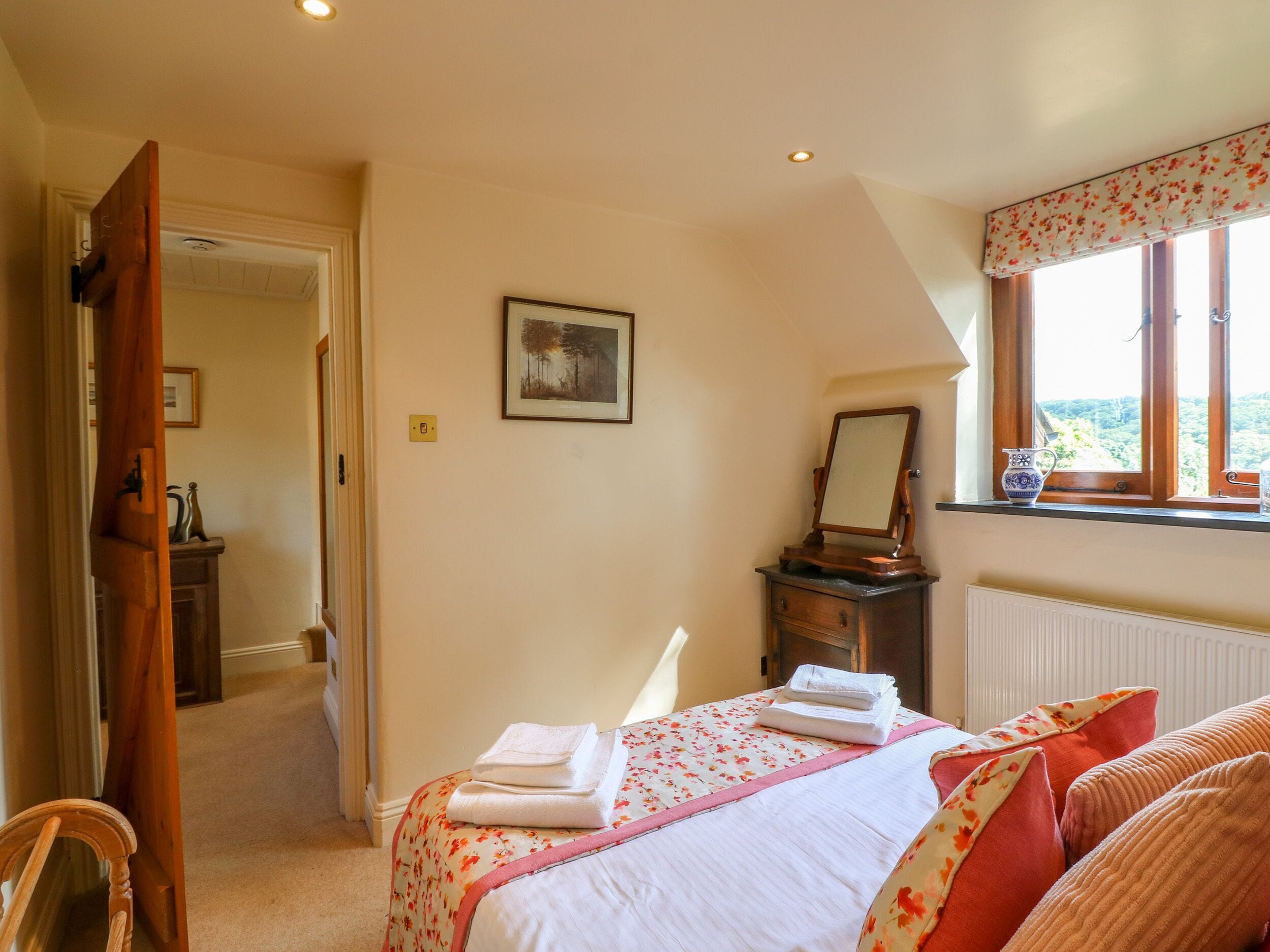 A bedroom with a bed, a dresser, a mirror, and a window with a view.