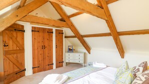 Ein Schlafzimmer mit schrägen Wänden, Holzbalken, einem Bett mit Kissen, einem Schminktisch und einem Kleiderschrank mit Schiebetür.