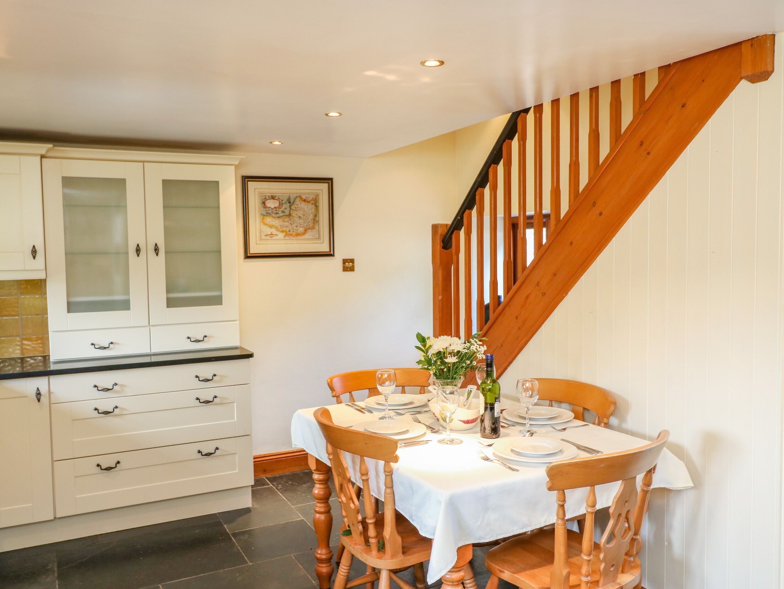 A dining area with a wooden staircase, white cabinets, and a table set for four.