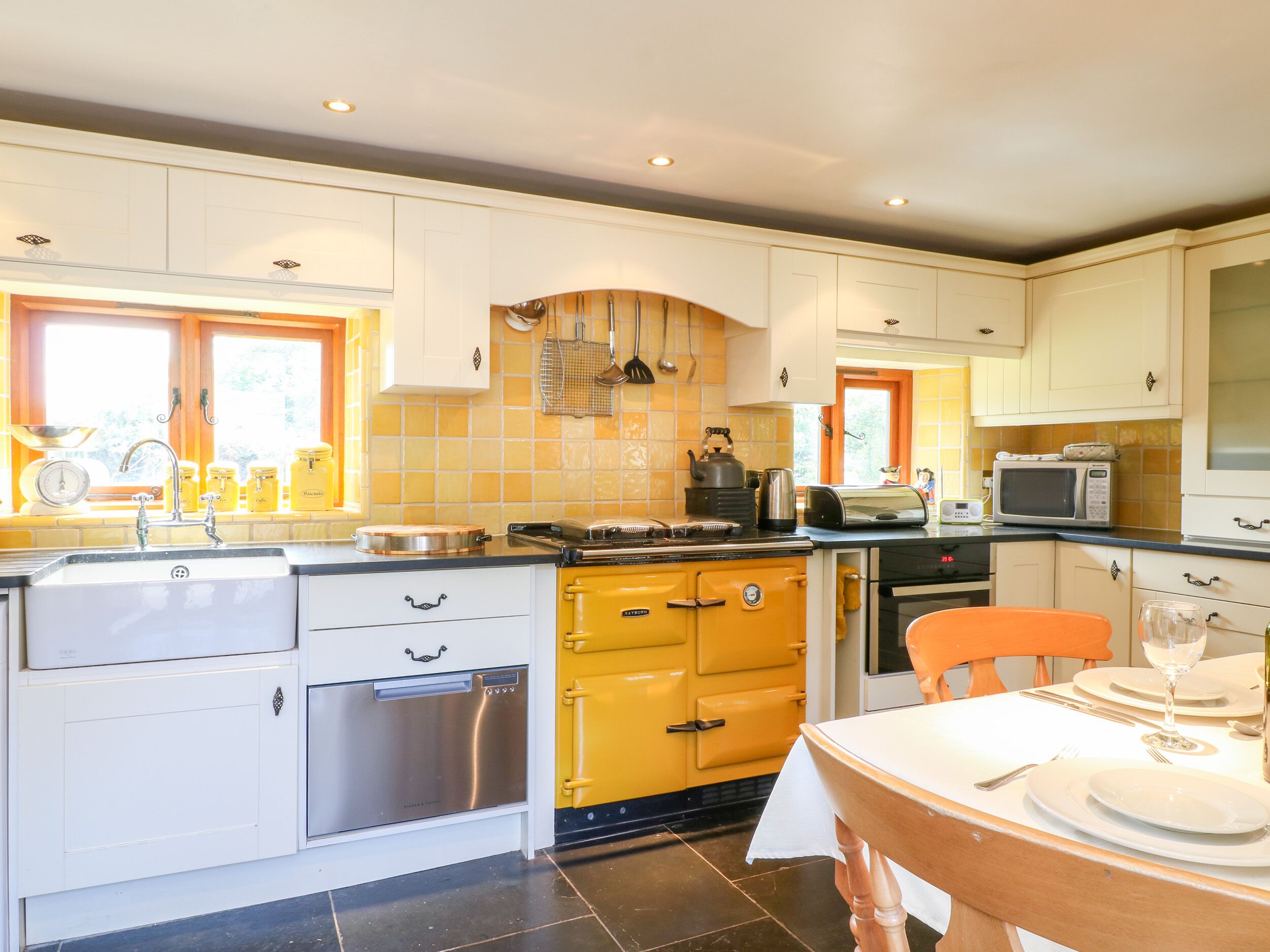 A kitchen with white cabinets, a yellow stove, and a dining table set for two.