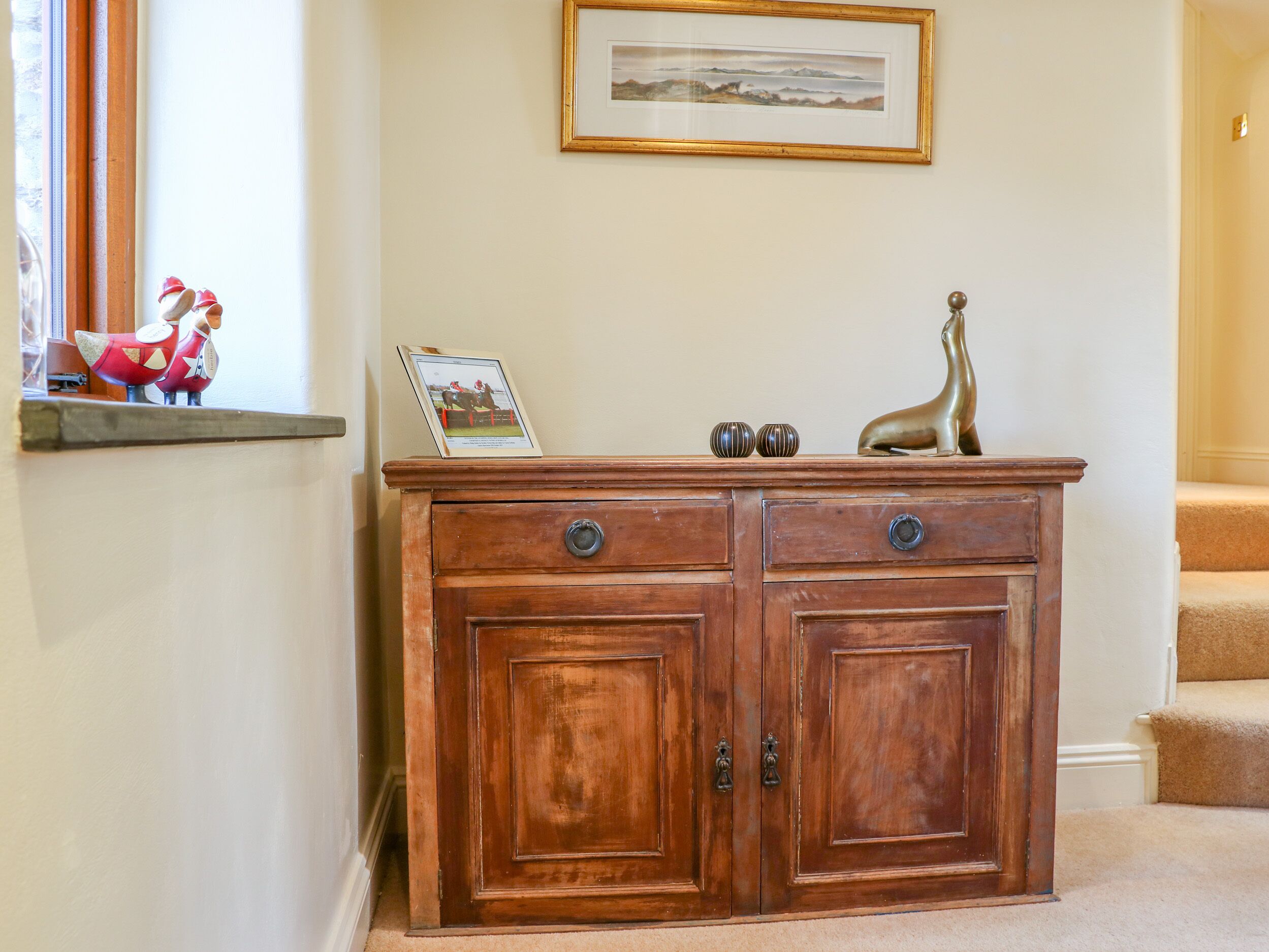 A wooden cabinet with two drawers and two doors, a framed picture on top, and decorative items on the shelf.