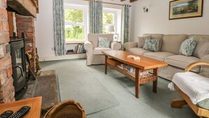 A cozy living room with a fireplace, two sofas, a wooden coffee table, and a bookshelf. - Barn House (Leyburn)