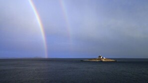Un faro en una pequeña isla, con un arcoíris al fondo.