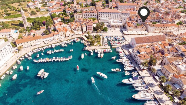 An aerial view of a coastal town with a marina filled with boats, historic buildings, and a prominent church tower.