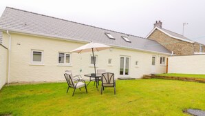 A house with a patio area featuring a table and chairs under an umbrella. - Hen Brynbedw (Llanybydder)