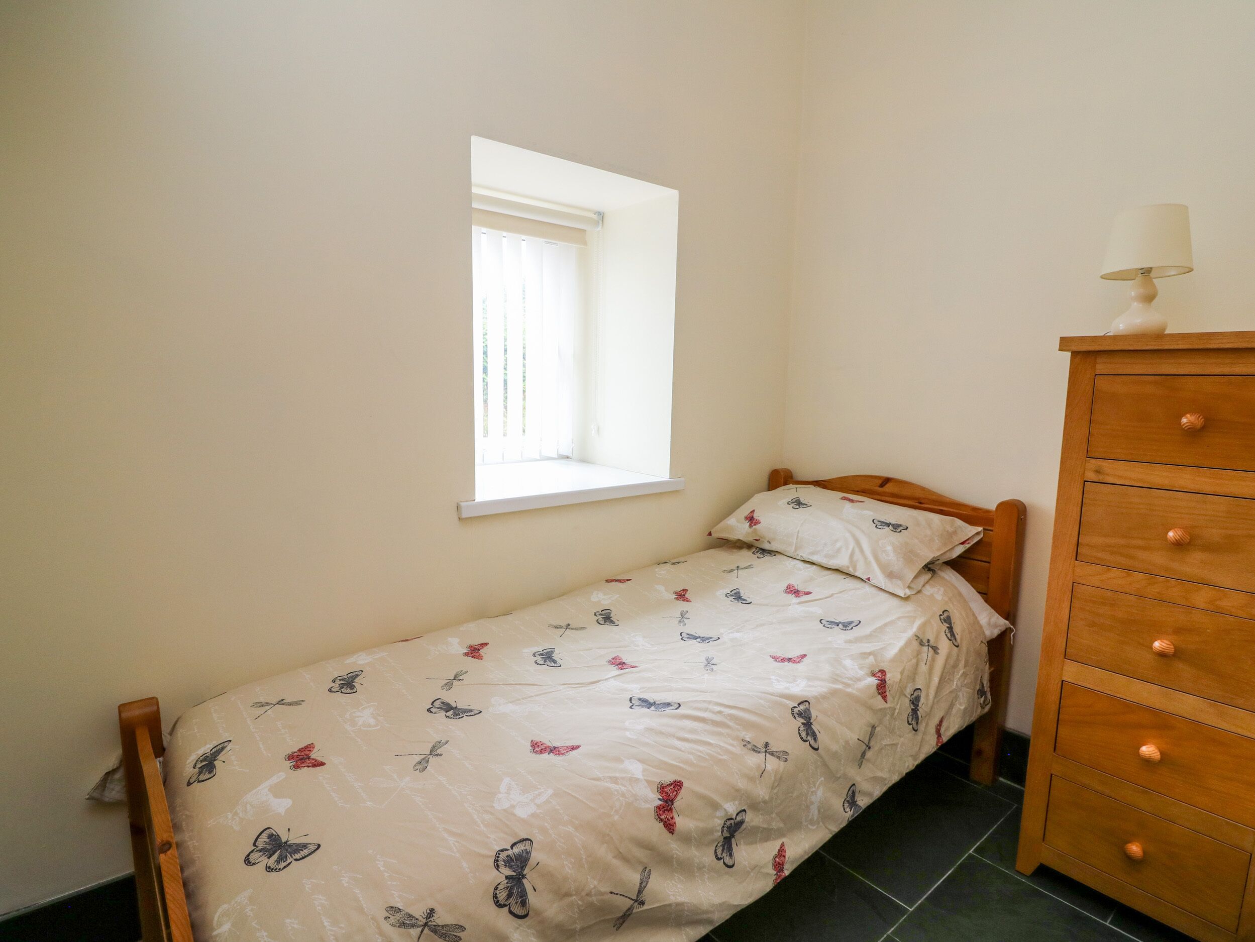 Ein kleines Schlafzimmer mit einem Einzelbett, einer Holzkommode und einem Fenster, das für natürliches Licht sorgt.