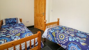 Two single beds with floral-patterned bedding in a room with a wooden door and white walls. - Hen Brynbedw (Llanybydder)