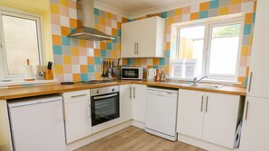 A compact kitchen with white cabinets, a microwave, a stove, and a dishwasher. - Hen Brynbedw (Llanybydder)