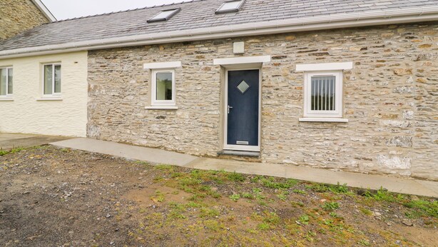 A stone building with a dark blue door, two windows with white frames, and a sloped roof with skylights. - Hen Brynbedw (Llanybydder)