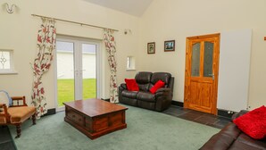 A living room with a brown leather sofa, a wooden coffee table, a wooden cabinet, and a view of the outside through a glass door. - Hen Brynbedw (Llanybydder)