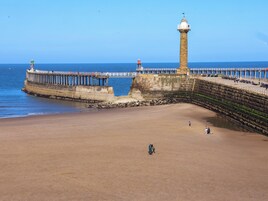 Escena costera con un faro, muelle y playa arenosa.