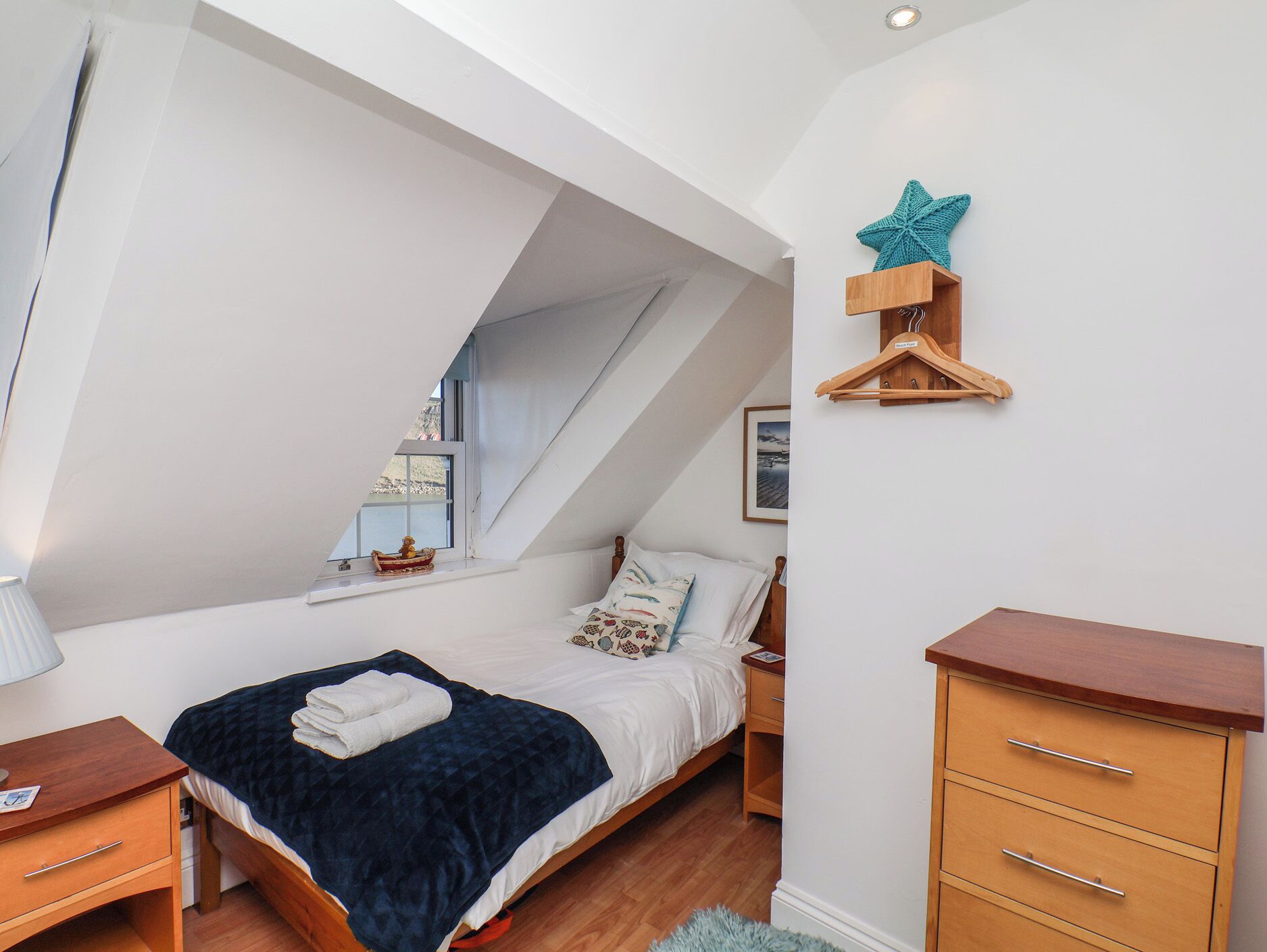 A bedroom with a sloped ceiling, a bed with a dark blue blanket, a wooden dresser, and a star decoration on the wall.