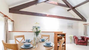A dining area with a round table set for four, surrounded by wooden chairs. A wooden bookshelf is against the wall, and a red leather sofa is visible in the background. - The Tallet (Dartmouth)