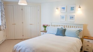 A bedroom with a large bed, a nightstand, a bedside table, a wardrobe, and a wall with framed pictures. - The Tallet (Dartmouth)