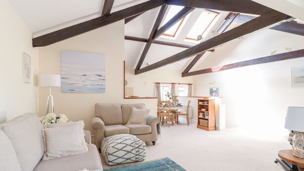 A cozy living room with a high ceiling, a sofa, a coffee table, and a dining area with a table and chairs. - The Tallet (Dartmouth)