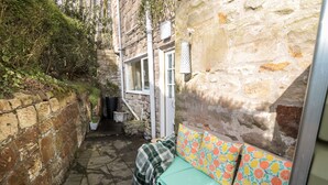 A narrow stone-walled courtyard with a bench and a small table. - Wordsworth Cottage West (Morpeth)