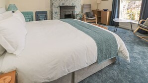 A bedroom with a large bed, a fireplace, a desk, and a window with curtains. - Wordsworth Cottage West (Morpeth)