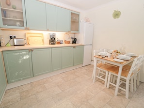 Una cocina con armarios verde claro, un refrigerador blanco, una mesa de comedor con sillas y un reloj de pared.