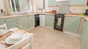 A kitchen with light green cabinets, a black oven, and a dining table set with white plates and glasses. - Wordsworth Cottage West (Morpeth)