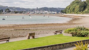 A coastal scene with boats, a sandy beach, and a grassy area with benches. - Mor Awel (Beaumaris)
