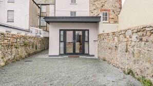 A modern building with a stone facade, a small entrance with a glass door, and a gravel driveway. - Mor Awel (Beaumaris)