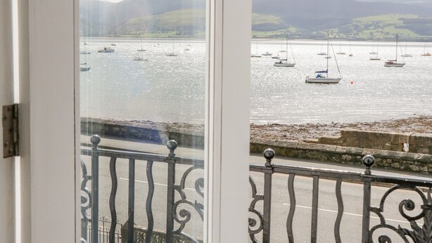 A view of a harbor with boats, a stone wall, and distant hills. - Mor Awel (Beaumaris)