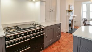 A modern kitchen with a gas stove, dark cabinetry, and a herringbone-patterned wooden floor. - Mor Awel (Beaumaris)