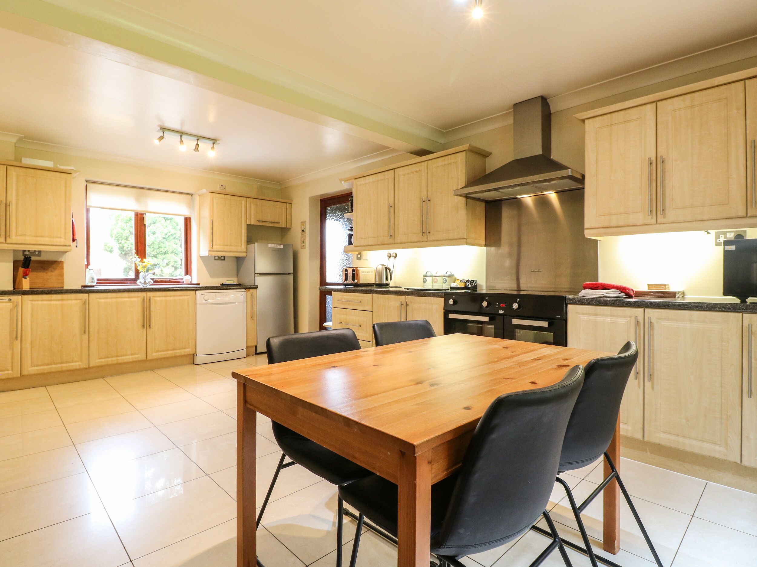 A modern kitchen with wooden cabinets, a stainless steel range hood, and a dining area with a wooden table and chairs.