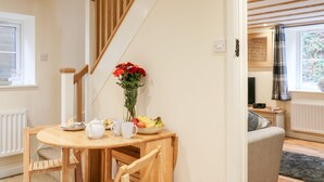 A dining area with a wooden table, chairs, and a vase of flowers. - Tilly's Cottage (Westbury)