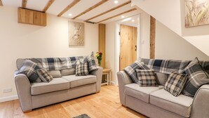 A modern living room with two grey sofas, wooden beams on the ceiling, a wooden door, and a painting on the wall. - Tilly's Cottage (Westbury)
