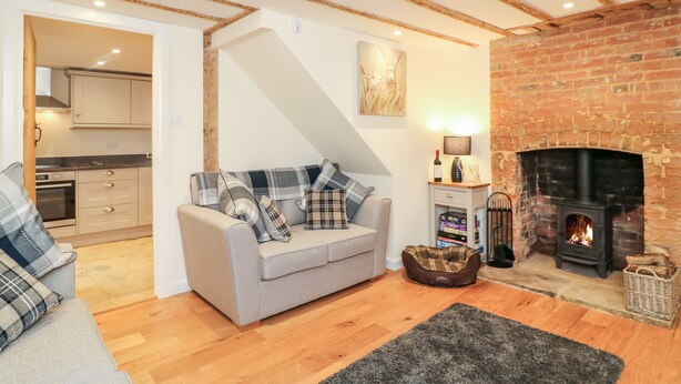 A cozy living room with a fireplace, a sofa with plaid cushions, and a pet bed. - Tilly's Cottage (Westbury)