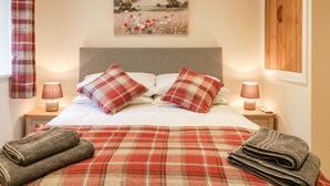A neatly made bed with plaid bedding, two bedside lamps, and a painting above it. - Tilly's Cottage (Westbury)