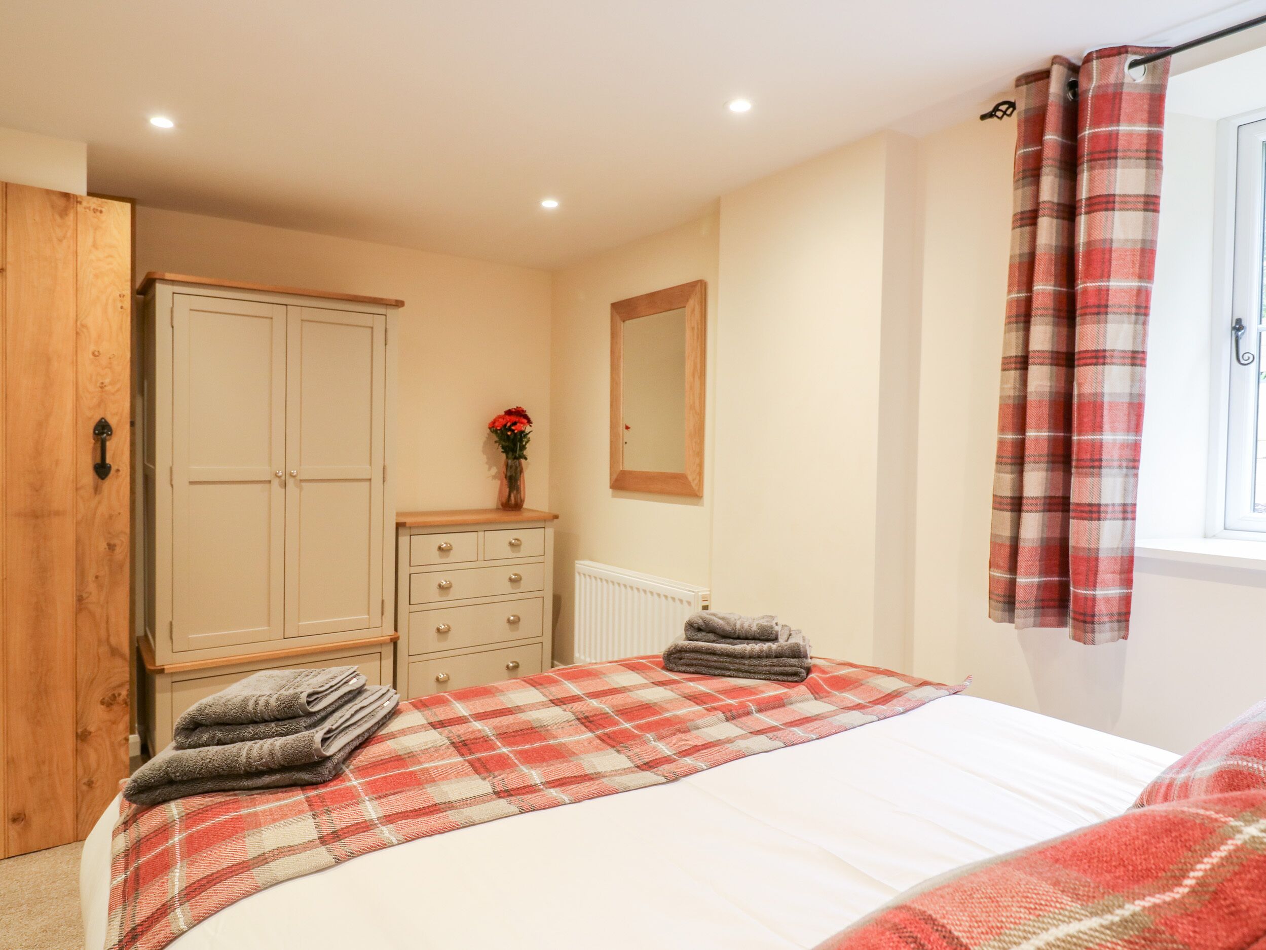 A bedroom with a bed, a wardrobe, a dresser, a radiator, a mirror, and a window with curtains.