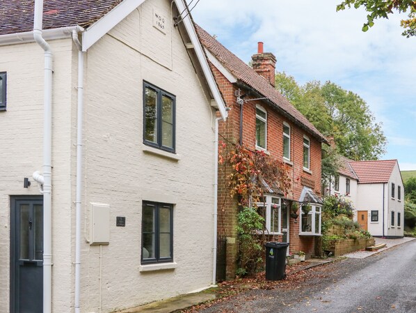 A row of traditional houses with brick and white walls, a clear sky, and a street with fallen leaves. - Tilly's Cottage (Westbury)