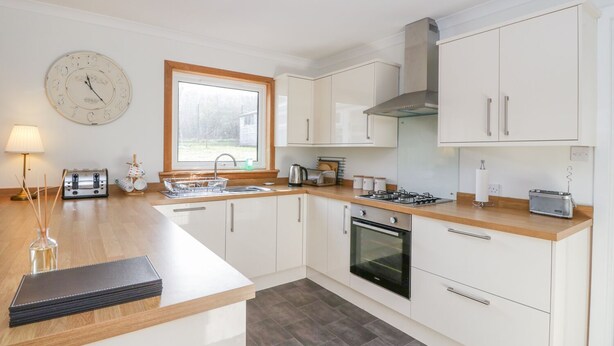 A modern kitchen with white cabinets, a wooden countertop, a built-in oven, a gas stove, and a window with a view of the outdoors. - Cromallt (Aberfeldy)