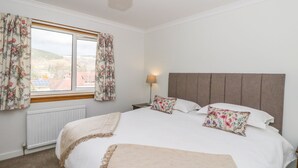 A bedroom with a large bed, floral curtains, a bedside lamp, and a view of the outdoors. - Cromallt (Aberfeldy)