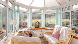 A conservatory with a glass ceiling, wicker furniture, and a view of a garden. - Cromallt (Aberfeldy)