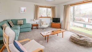 A living room with a green sofa, a wooden coffee table, a white armchair, and a television. - Cromallt (Aberfeldy)