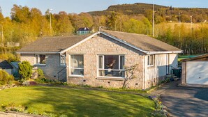 A stone house with a sloped roof, a garage, and a well-maintained lawn. - Cromallt (Aberfeldy)