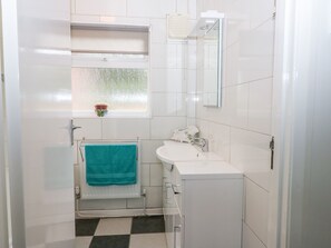 A small, compact bathroom with a white sink, a mirror, and a window with a view of the outside. - Glynde (Dover)