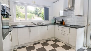 A modern kitchen with white cabinets, a black and white checkered floor, a window with a view of greenery, and a toaster on the counter. - Glynde (Dover)