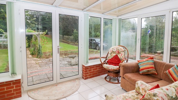A sunroom with a glass door leading to a garden, a wicker chair, and a sofa with floral cushions. - Glynde (Dover)
