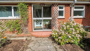 A brick house with a glass door entrance, a small garden with hydrangeas, and a solar panel on the roof. - Glynde (Dover)