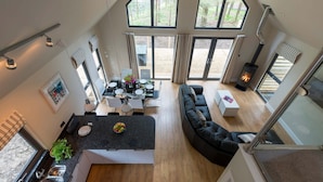 A modern interior with a dining area, black leather sofa, and a wood-burning stove. - Bracken Howe Lodge (Whitby)